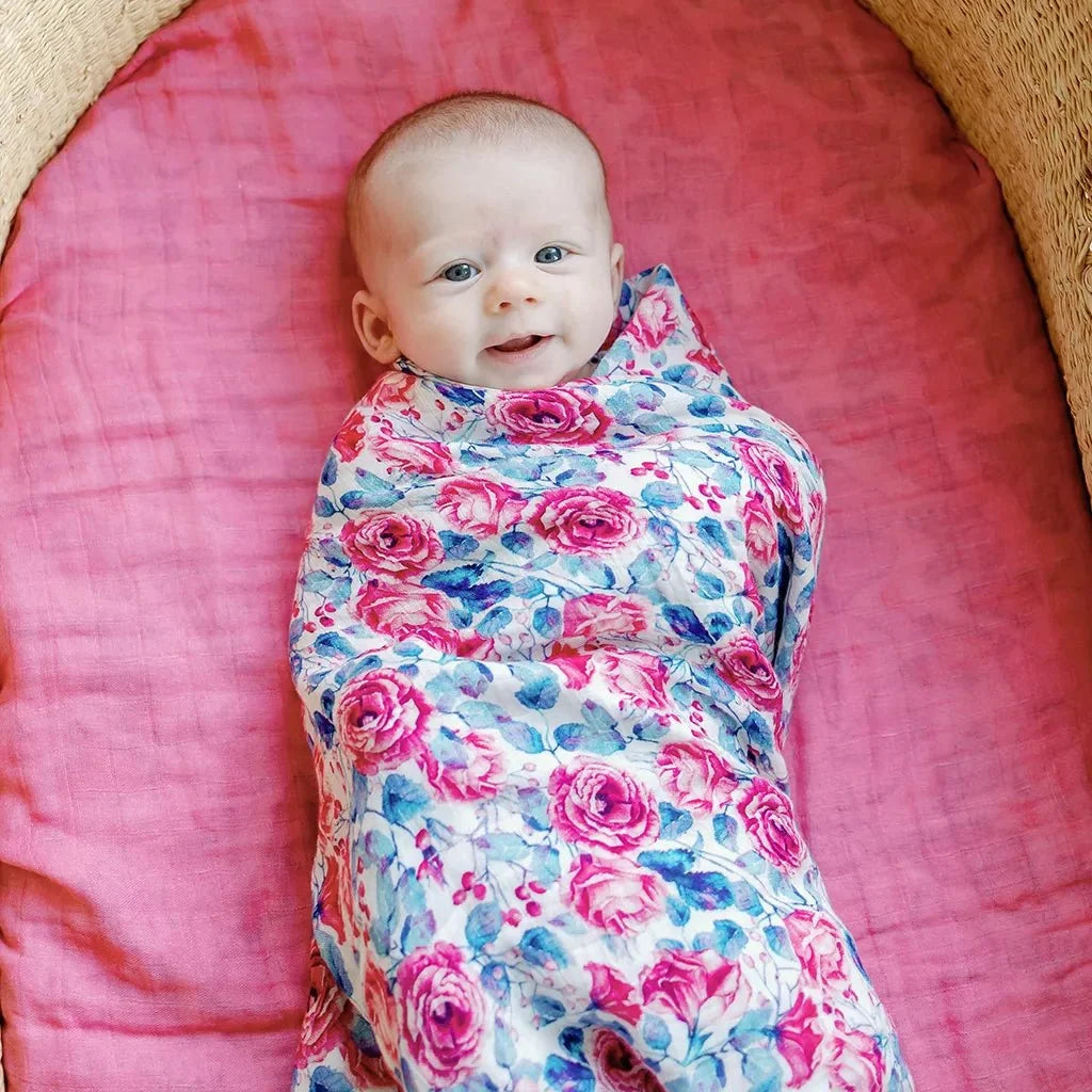 Smiling baby wrapped in a pink and blue floral muslin swaddle in a woven basket