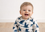 Baby wearing a blue and white onesie with bird pattern on a beige carpet.