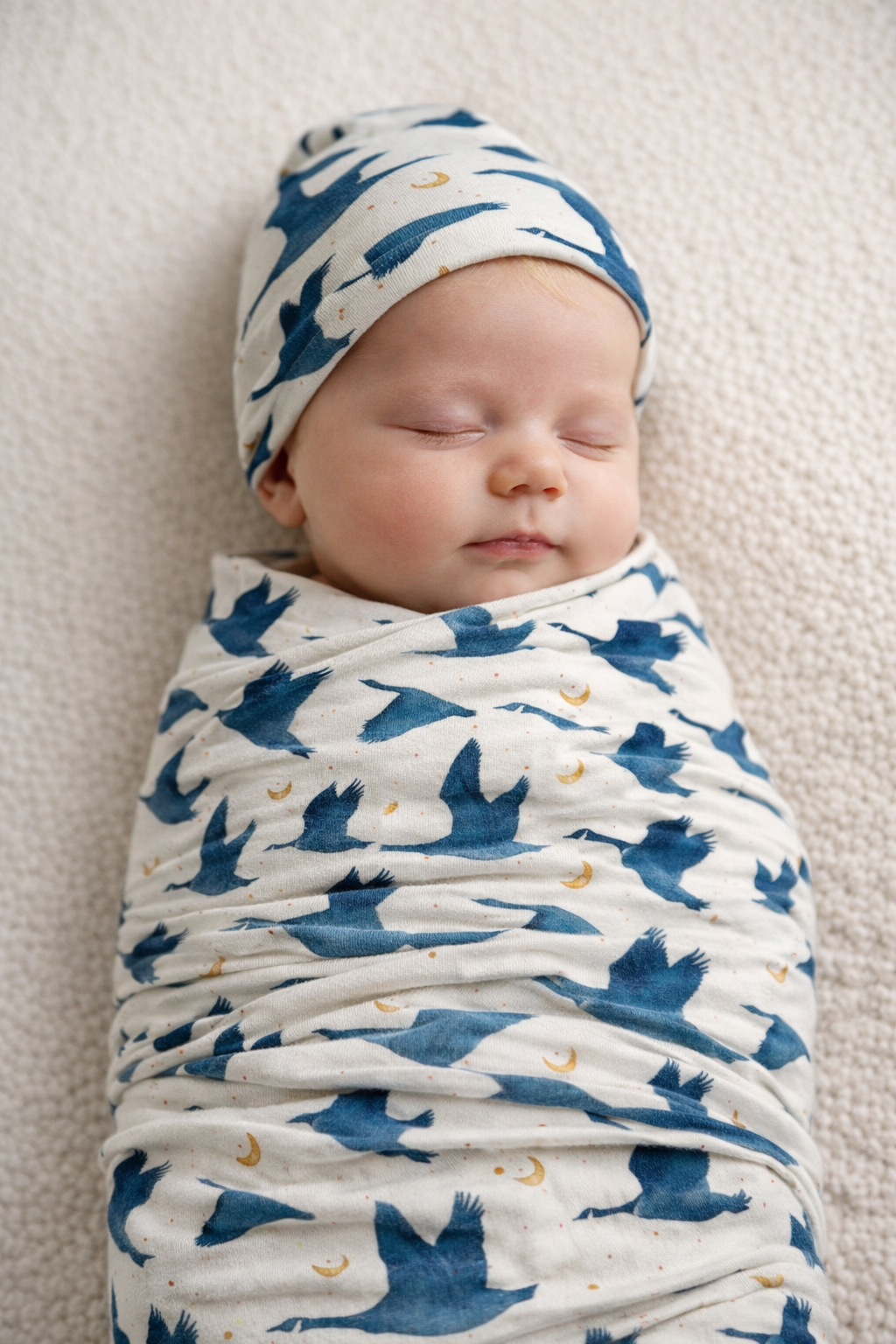 Newborn baby in Gus goose print stretchy swaddle and matching beanie, TENCEL Modal swaddle set